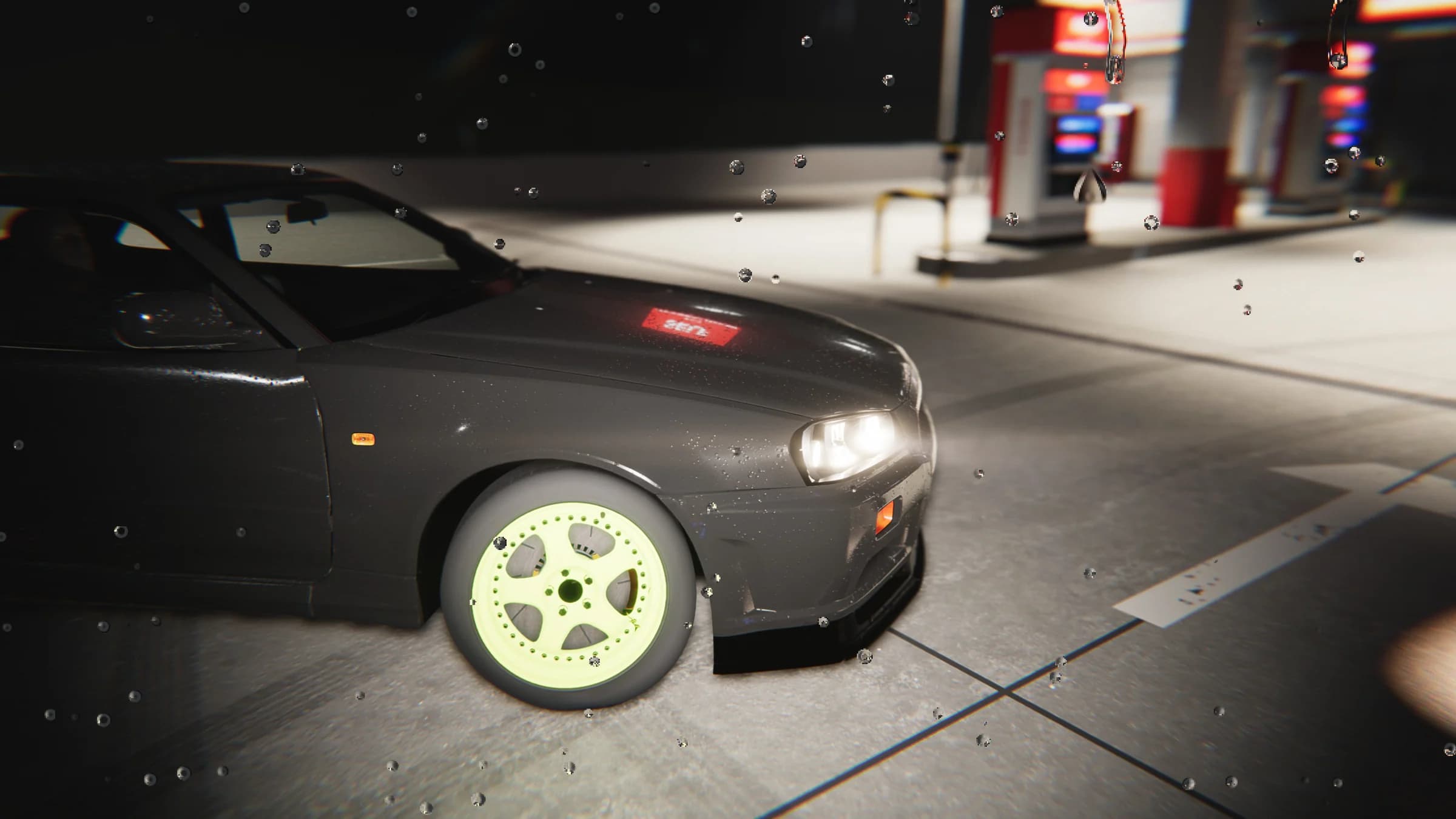 Close front-quarter view of the dark coupe and its lime-green front wheel beside the fuel pumps