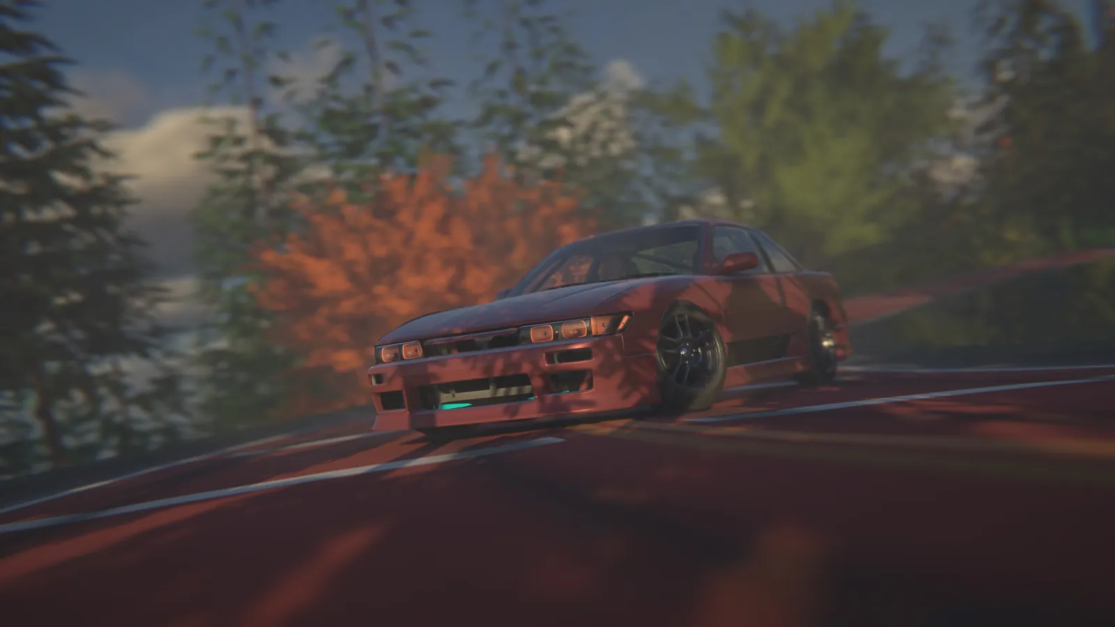 Red coupe sliding through a corner on a forested road with an orange autumn tree behind it