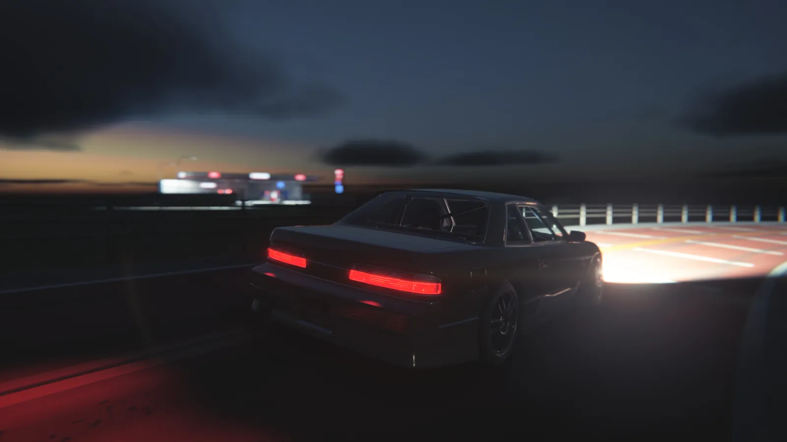 Rear view of a silver coupe with glowing red tail lights on a dark highway, with a lit fuel station in the distance at dusk